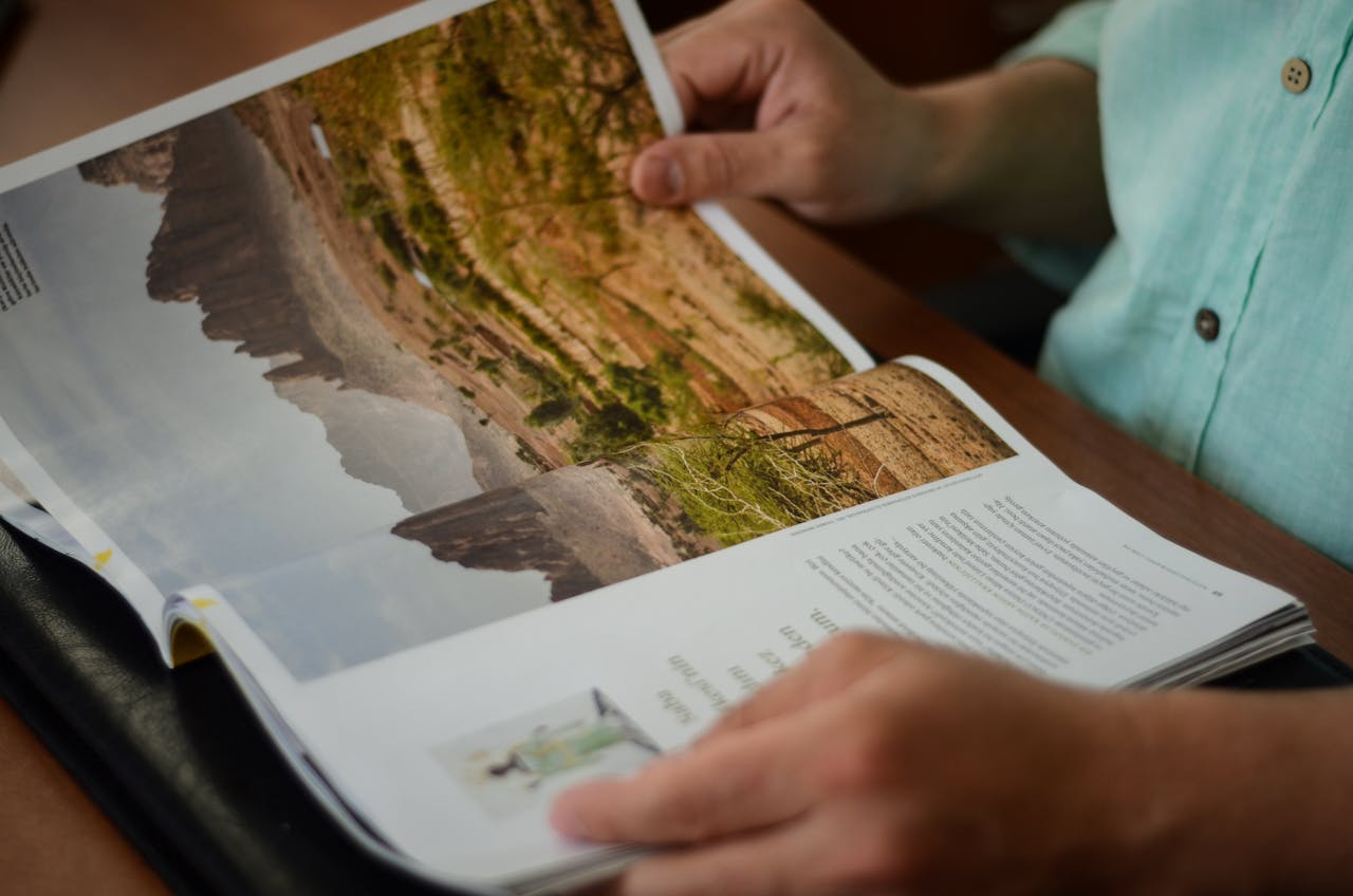 Close-up of a man reading a magazine indoors, focusing on hands and pages.